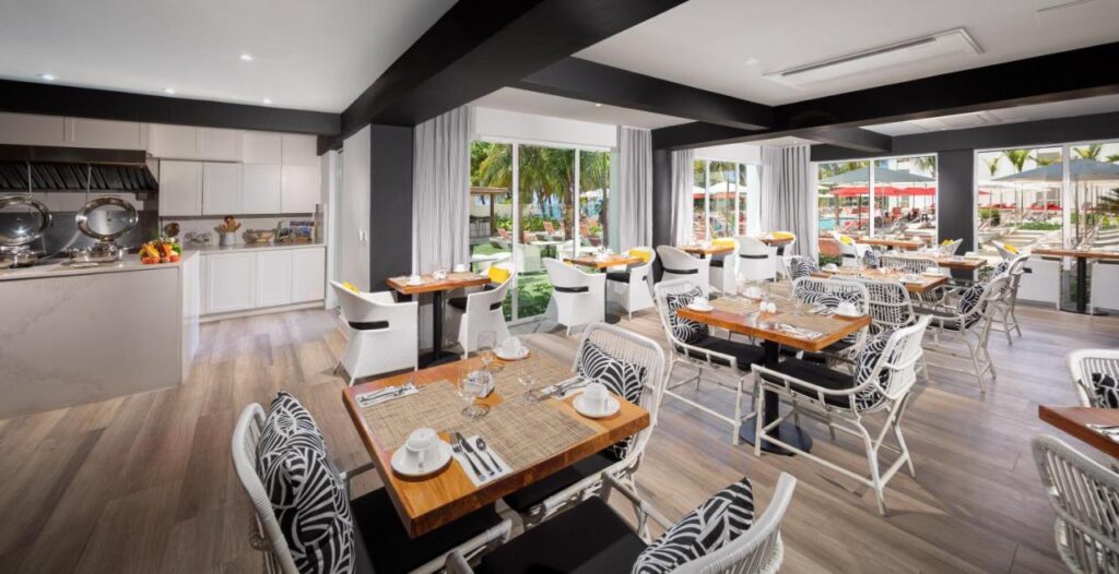 Um interior de restaurante moderno no S Hotel Montego Bay com cadeiras com estampa de zebra, mesas de madeira e vista para uma área de piscina com espreguiçadeiras e guarda-sóis.