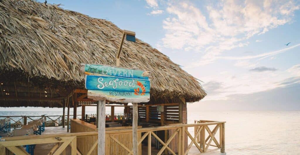 Um restaurante de frutos do mar com teto de palha à beira-mar no Mangrove Beach Corendon, uma área de estar aconchegante e uma placa com os dizeres "Taverna à Beira-Mar".