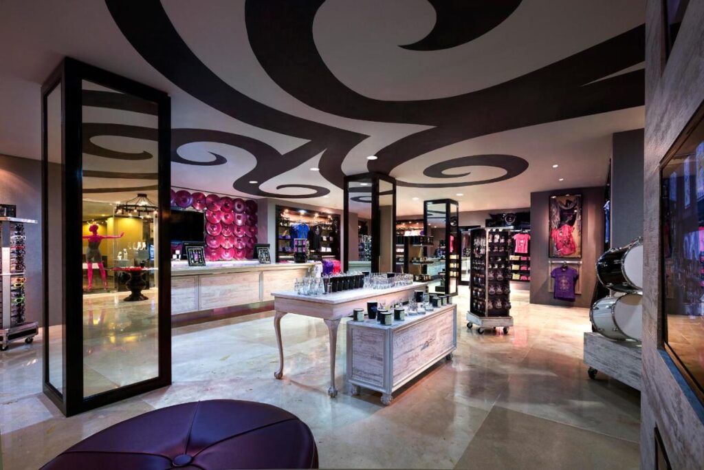Interior de uma loja moderna com redemoinhos decorativos no teto, vários produtos nas prateleiras e uma mesa central de exposição no Hard Rock Hotel Cancun.