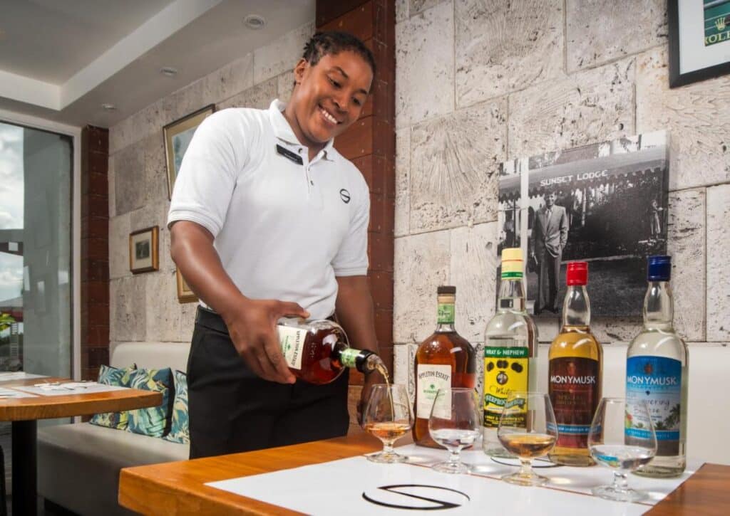 Uma pessoa serve rum em um copo em uma mesa com várias garrafas de rum em um restaurante do S Hotel Montego Bay.