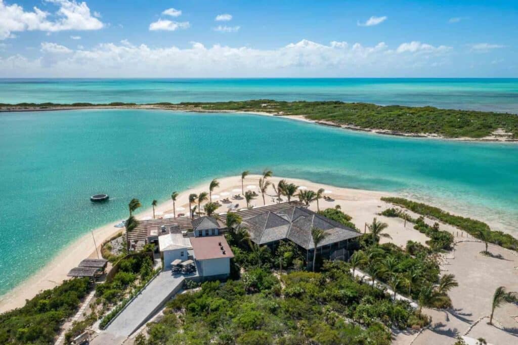 Vista aérea do Ambergris Cay Private Island com edifícios, palmeiras e um mar azul-turquesa sob um céu azul claro. Esse é um dos melhores resorts all inclusive no Caribe.