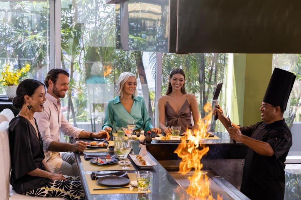Um chef cozinha em uma mesa de teppanyaki com chamas, enquanto quatro pessoas assistem e sorriem em um restaurante do Hyatt Zilara Cancun. Esse é um dos melhores resorts all inclusive no Caribe.
