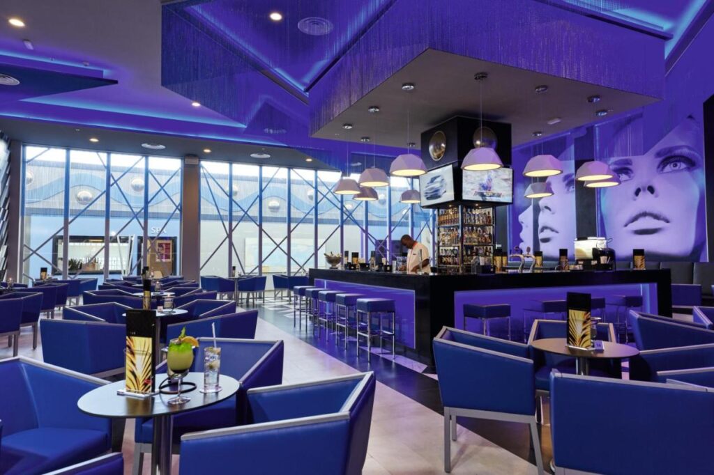 Um bar moderno do Riu Palace Paradise Island com iluminação azul, móveis contemporâneos e grandes obras de arte com temas de rostos. Esse é um dos melhores resorts all inclusive no Caribe.