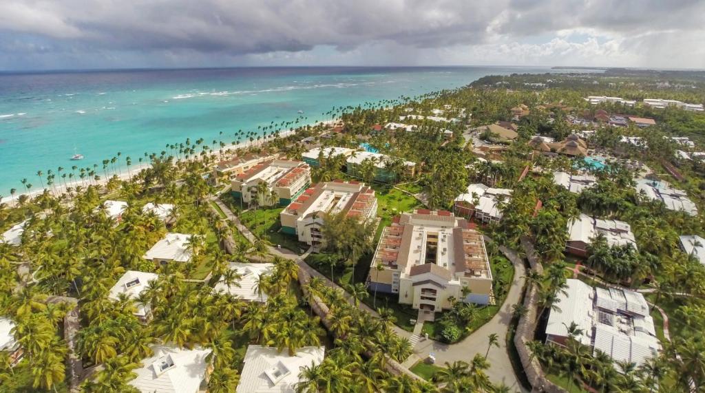 Vista aérea do Grand Palladium Bavaro Suites Resort & Spa à beira-mar com vários edifícios, palmeiras e um oceano azul-turquesa sob um céu nublado. Esse é um dos melhores resorts all inclusive no Caribe.