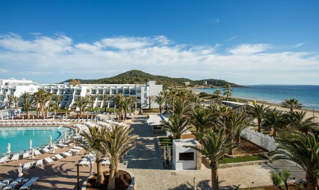 O Grand Palladium White Sand Resort & Spa com uma grande piscina, inúmeras palmeiras e edifícios brancos, localizado ao lado de uma praia arenosa com céu limpo. Esse é um dos melhores resorts all inclusive no Caribe.
