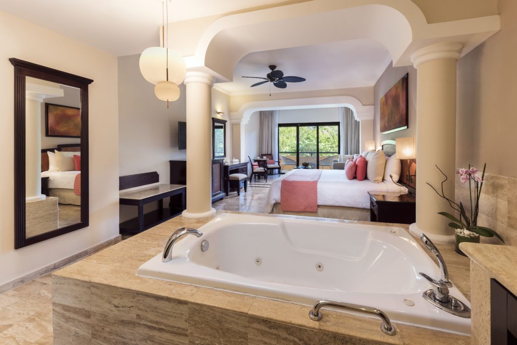 Quarto do Grand Palladium White Sand Resort & Spa com cama grande, área de estar e banheira de hidromassagem interna. O quarto tem varanda com vista para a vegetação.