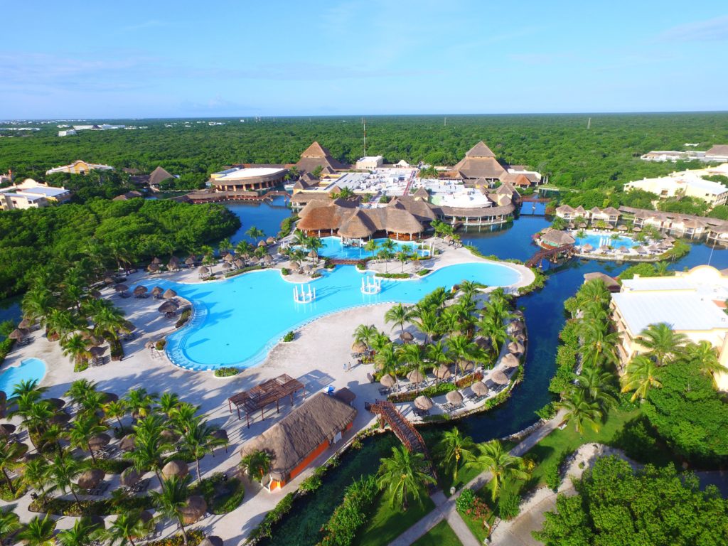 Vista aérea do Grand Palladium White Sand Resort & Spa com grandes piscinas azuis, edifícios com telhados de palha e arredores verdejantes. Esse é um dos melhores resorts all inclusive no Caribe.