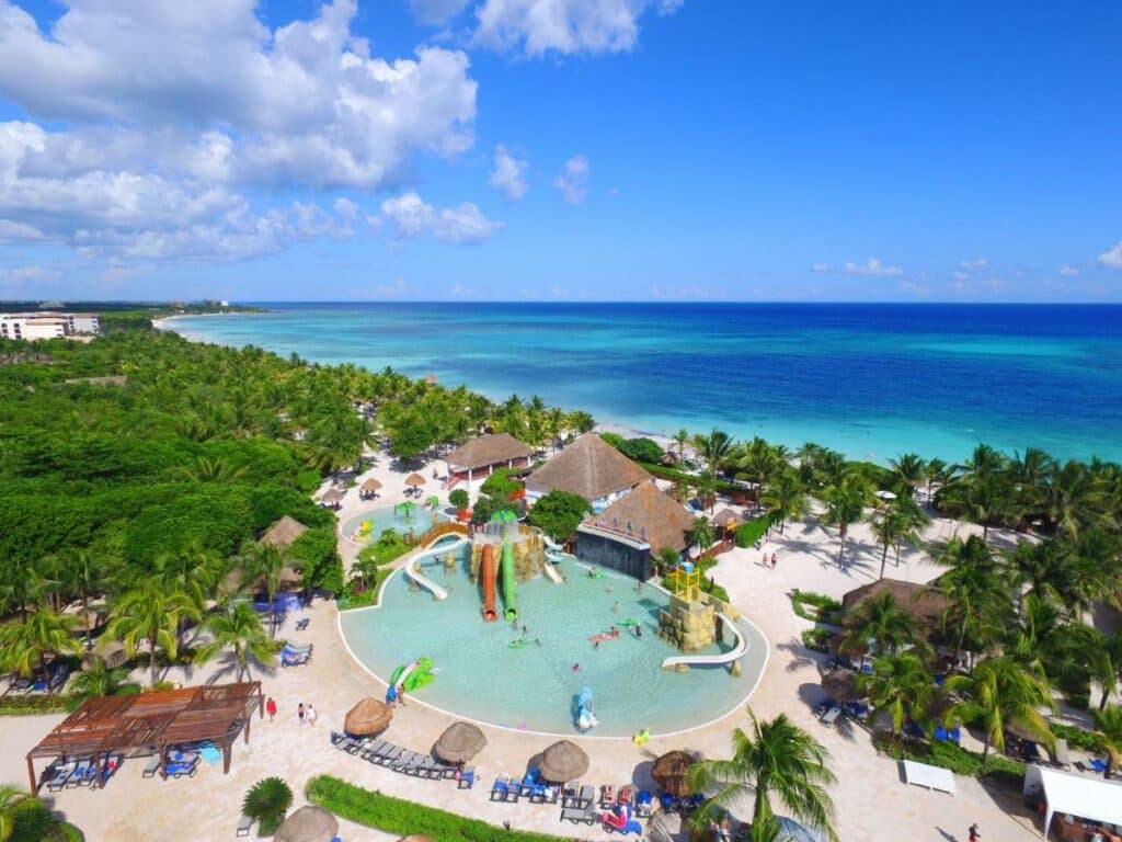 Vista aérea do Grand Palladium Colonial Resort & Spa com uma grande piscina, toboáguas, palmeiras, espreguiçadeiras e um oceano azul-turquesa ao fundo. Esse é um dos melhores resorts all inclusive no Caribe.