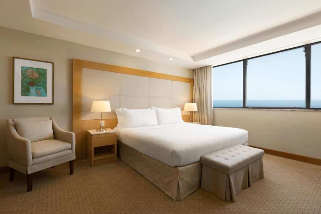 Quarto do Hilton Copacabana Rio de Janeiro com uma cama de casal, janela ampla, uma poltrona e duas mesas de cabeceira com abajures, para representar onde ficar em Copacabana.
