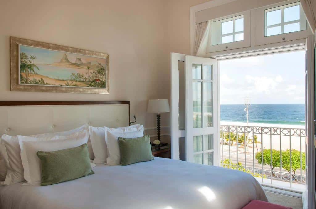 Um quarto no Coapcabana Palace com uma cama feita, portas de varanda abertas, vista para o mar e uma pintura de paisagem acima da cabeceira, para representar onde ficar em Copacabana.