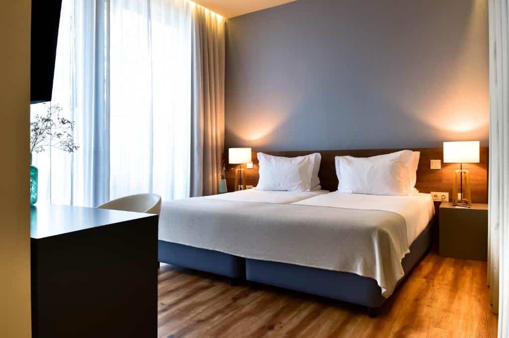 Quarto de hotel com duas camas de solteiro bem arrumadas, uma escrivaninha, cadeira, mesas de cabeceira e iluminação suave. Esta é uma das indicações onde ficar no Algarve.