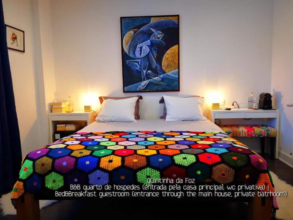 Uma cama com um cobertor de crochê colorido, mesas de cabeceira com luminárias e arte na parede em um quarto de hóspedes aconchegante.