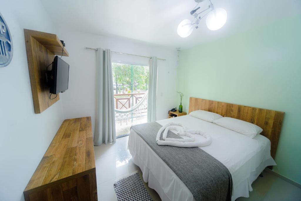 Um quarto com uma cama de casal, TV, móveis de madeira, parede verde-clara e uma varanda com uma rede do lado de fora, na Pousada Toca dos Aventureiros, para representar pousadas em Barreirinhas.
