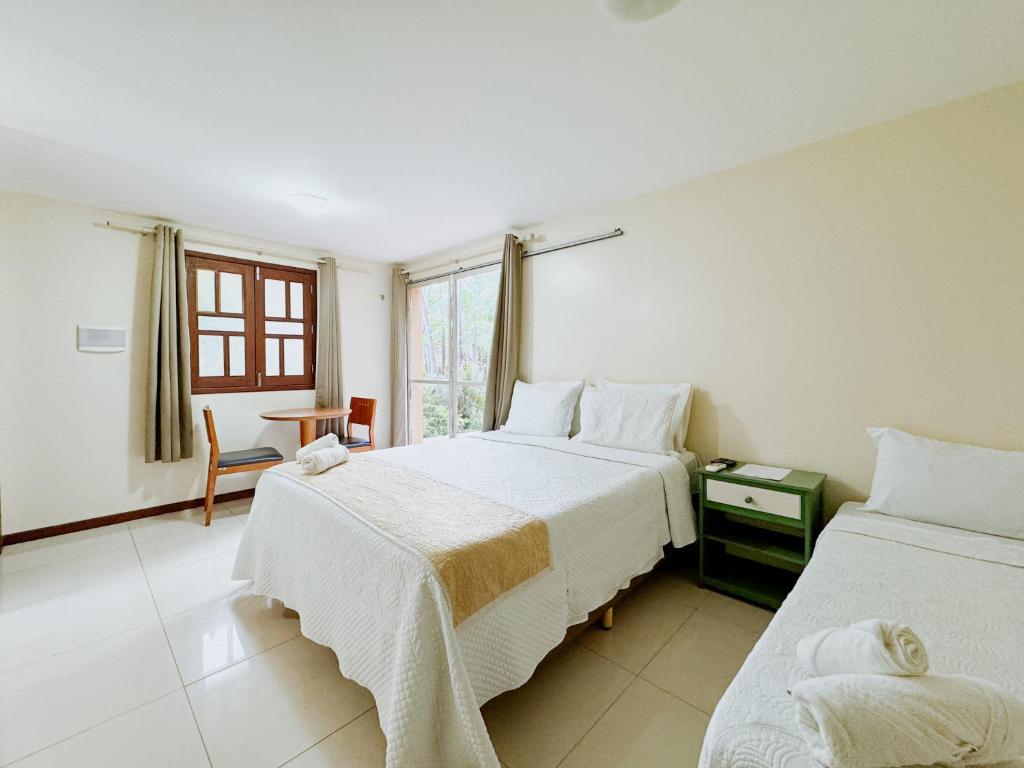 Um quarto na Pousada Boa Vista bem iluminado com duas camas, uma janela, uma escrivaninha e uma cadeira, piso de azulejos, paredes e cortinas de cores claras, para representar pousadas em Barreirinhas.