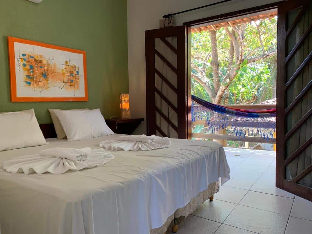 Uma cama bem arrumada em um quarto com uma porta aberta que dá para uma varanda com uma rede e vista para as árvores do lado de fora, na Pousada do Rio Barreirinhas, para representar pousadas em Barreirinhas.