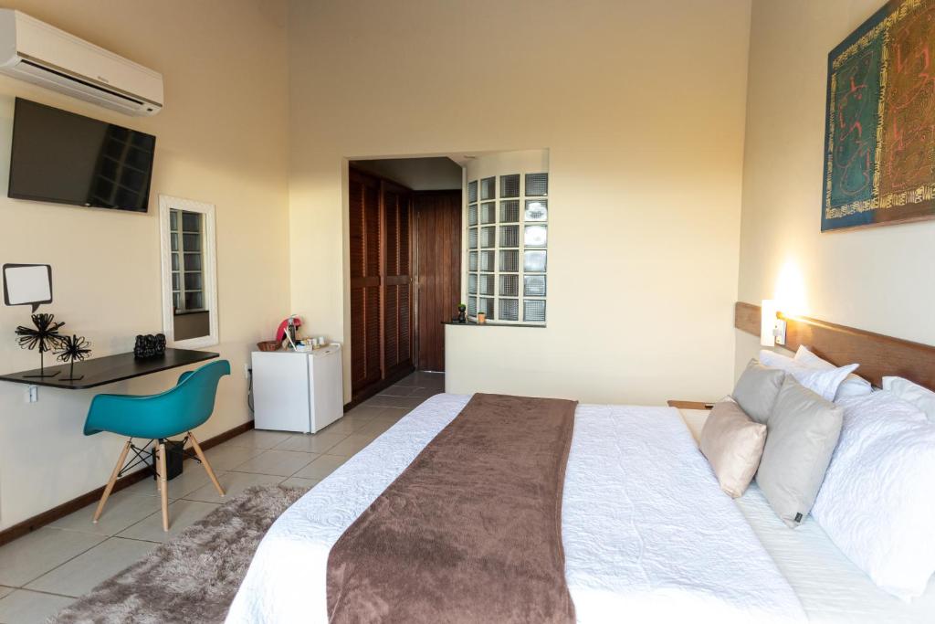 Um quarto moderno na Pousada Amancay na Praia João Fernandes, com uma cama de casal, escrivaninha, cadeira, TV de parede, frigobar e portas de armário de madeira, para representar pousadas em Búzios.