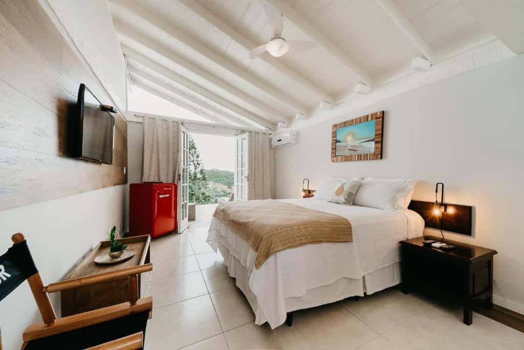 Quarto do Baía do João Eco Pousada com uma sacada dando vista pra natureza, uma cama de casal, móveis de madeira rústica, uma televisão e um frigobar grande, para representar pousadas em Búzios.