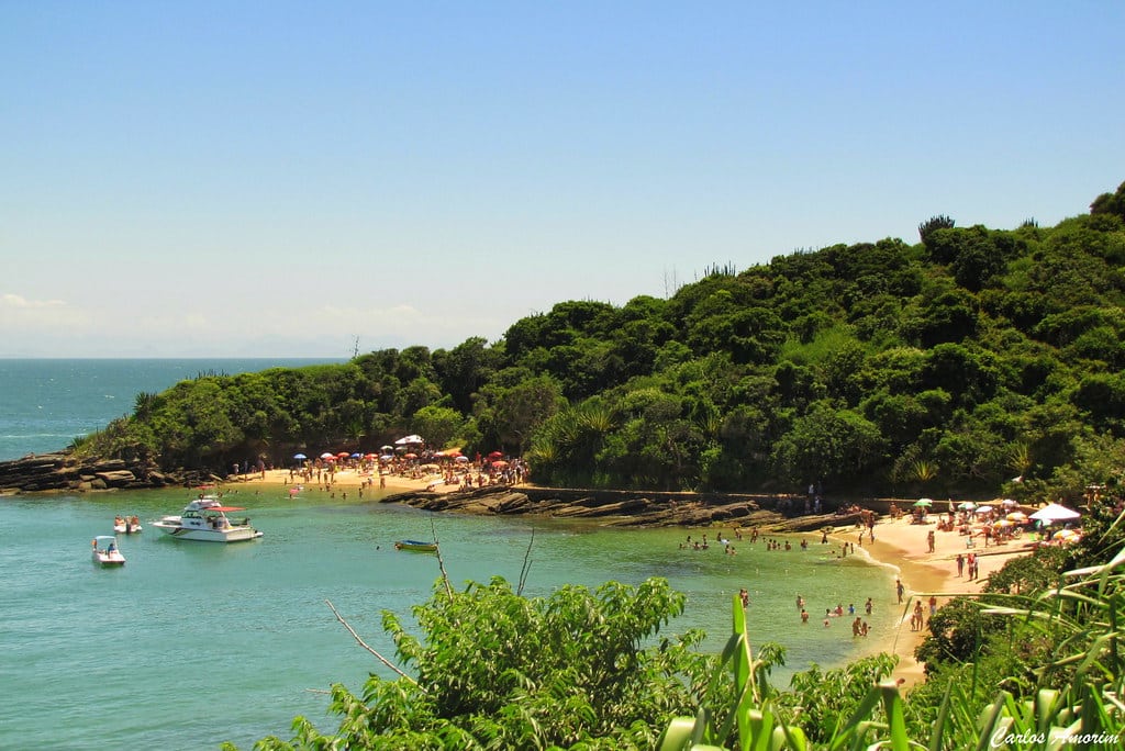 Vista da Praias Azeda e Azedinha. Um pouco de árvores na frente, atrás a vista das duas praias com bastante pessoas e duas lanchas no mar.