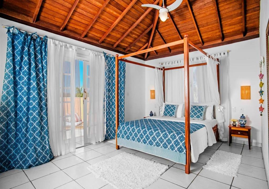 Um quarto na Villa Baobá na Praia da Ferradura com uma cama de dossel, roupa de cama com estampa azul, paredes brancas, piso de azulejo e cortinas com estampa azul, para representar pousadas em Búzios.
