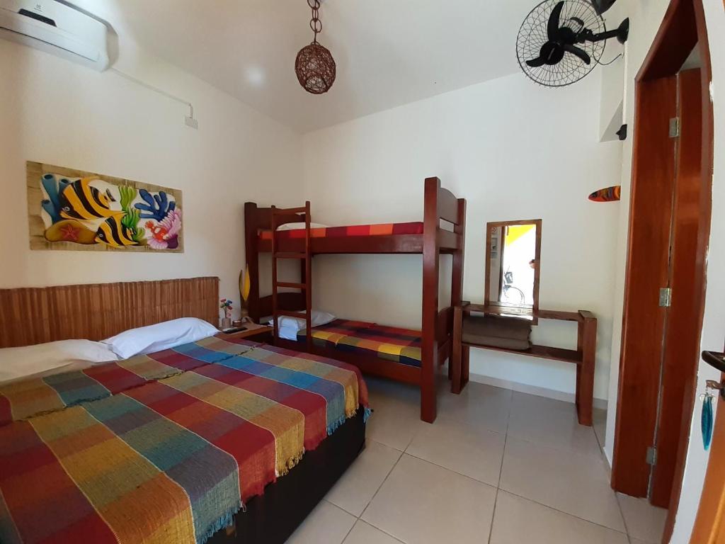 Um quarto no A Ver o Mar Beach House (Cocanha) com uma cama de casal e um beliche, ambos com cobertores coloridos, um espelho, uma escrivaninha e arte na parede, para representar pousadas em Caraguatatuba.