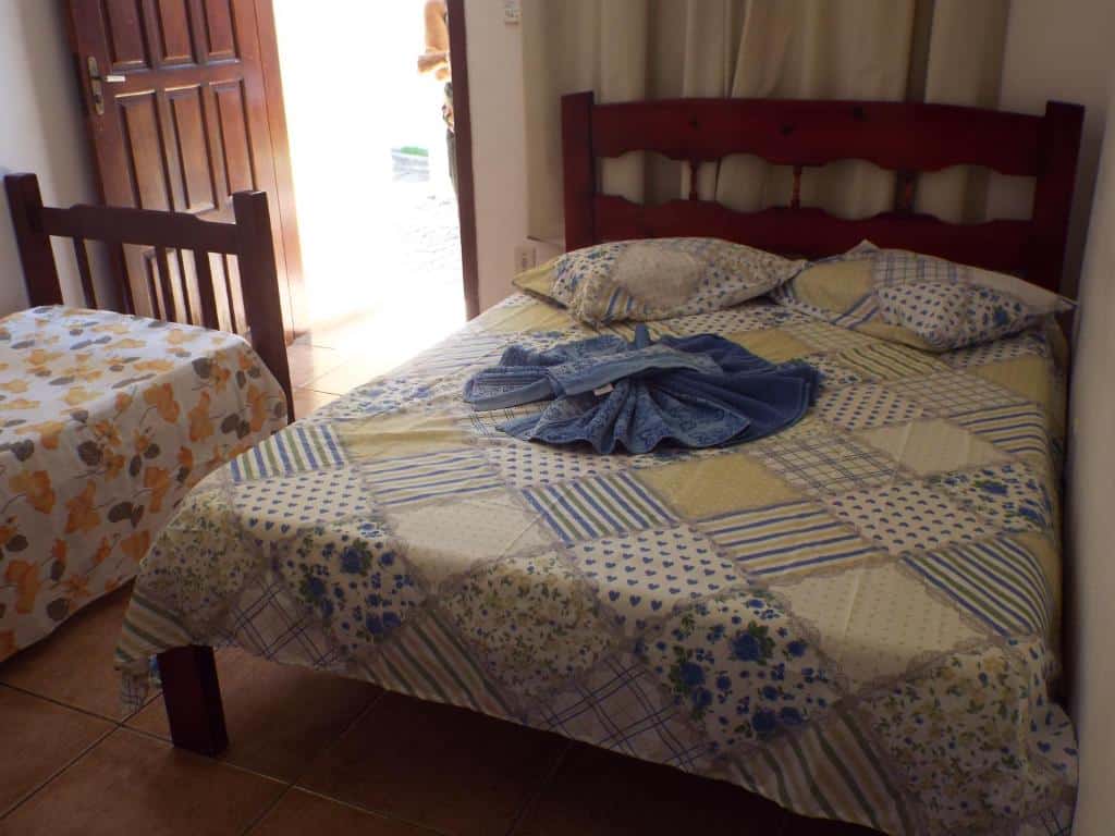 Cama de casal com lençol, travesseiros e toalhas arrumadas, além de uma cama de solteiro bem de frente para a porta, na Pousada Marambaia (Praia das Palmeiras).