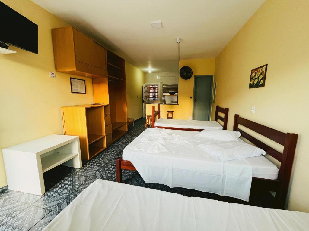 Um quarto na Pousada Caraguá (Martim de Sá) com duas camas de solteiro, móveis de madeira, uma pequena escrivaninha e vista para uma cozinha nos fundos, para representar pousadas em Caraguatatuba.