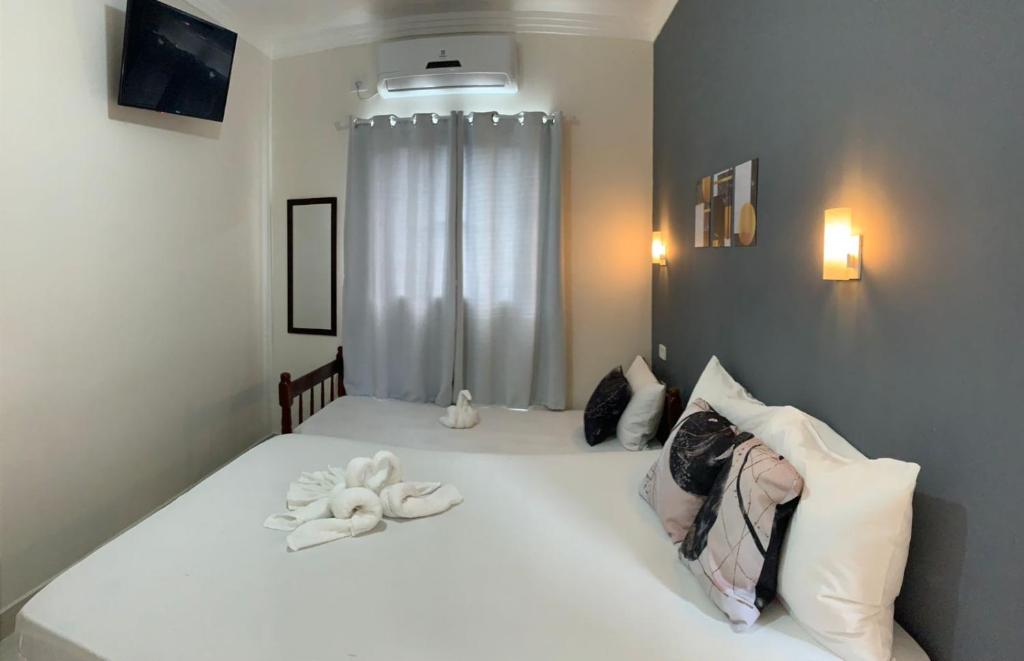 Quarto pequeno na Pousada Recanto Som do Mar (Massaguaçu) com duas camas, parede cinza com detalhes, TV na parede, ar-condicionado e toalhas dobradas em forma de cisne, para representar pousadas em Caraguatatuba.