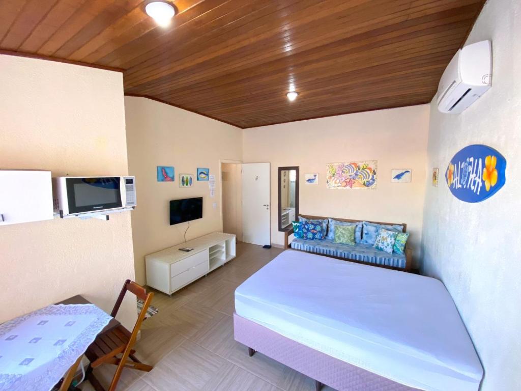 Um quarto estúdio no Barreto Hospedagem (Massaguaçu) bem iluminado com uma cama, sofá, TV, micro-ondas, mesa, arte na parede e teto com painéis de madeira, para representar pousadas em Caraguatatuba.