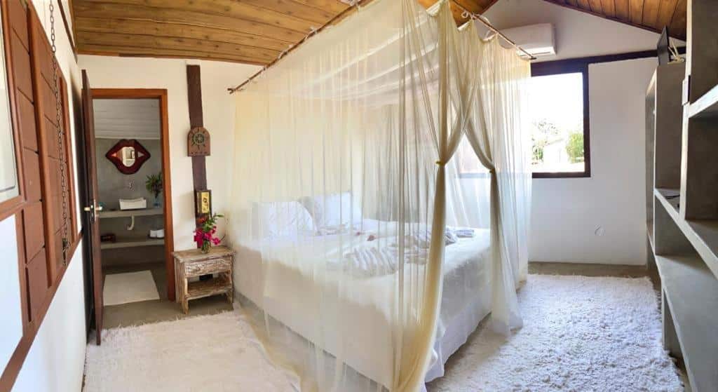 Um quarto da Pousada Caraiva Guest House com uma cama de dossel coberta por cortinas transparentes, um teto de madeira e uma janela que permite a entrada de luz natural.
