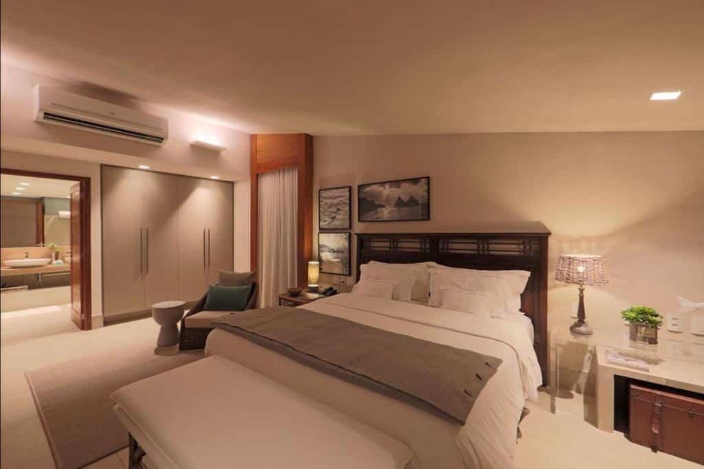 Quarto de casal espaçoso na Pousada Zé Maria, em Fernando de Noronha, com cama grande, mesa de cabeceira com abajures diferentes, armário e banheiro ao fundo