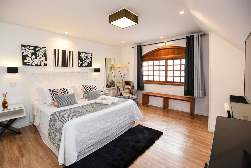 Quarto espaçoso com uma cama grande, poltrona, banco na janela, piso de madeira e detalhes de decoração moderna, na Pousada La Lavande, para representar pousadas em Gramado.