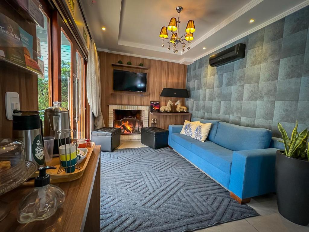 Lounge da Pousada Viena com um sofá de dois lugares na parede direita e um ar-condicionado preto preso acima do sofá, há também uma lareira com fogo aceso, uma televisão de tela plana acima e um lustre preso no teto. No canto esquerdo inferior da imagem é possível ver uma mesinha com cafeteira e garrafas térmicas, além de algumas xícaras coloridas, na Pousada Viena.
