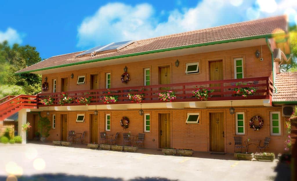 Vsta frontal da Pousada Mikolay mostrando uma construção de dois andares com paredes de tijolos e janelas verdes.