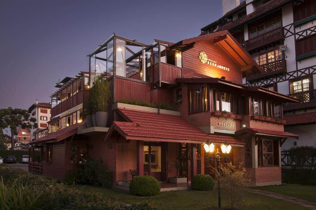Vista frontal da Pousada Bernardete em Gramado ao entardecer. A construção conta com três andares e um terraço aberto com teto de vidro