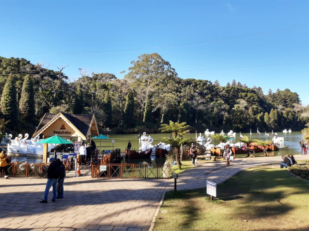 Entrada do parque Lago Negro, em Gramado, com vista para o porto do lago onde ficam vários pedalinhos em formato de cisne branco. O céu está azul claro e sem nuvens