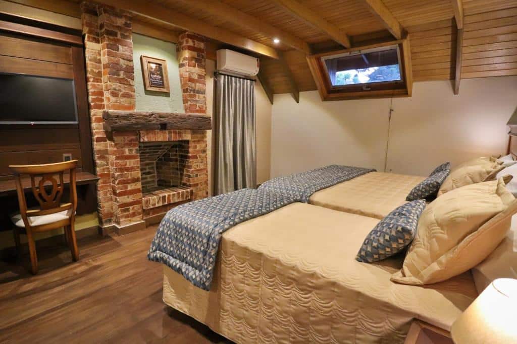 Suíte da Pousada Serra Paradiso com duas camas de solteiro unidas no lado direito do quarto, uma lareira em frente as camas e uma porta acortinada no canto, para representar pousadas em Gramado.