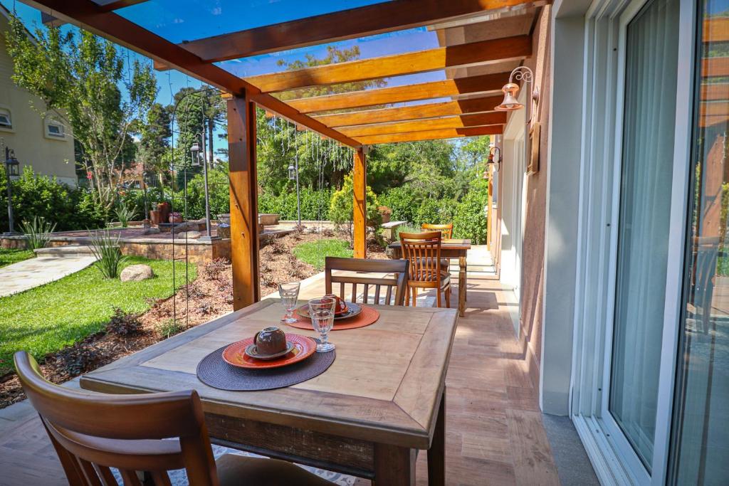 Área externa do refeitório com vista para o jardim, há duas mesas quadradas de madeiras com duas cadeiras em cada uma, na propriedade da Pousada Serra Paradiso.