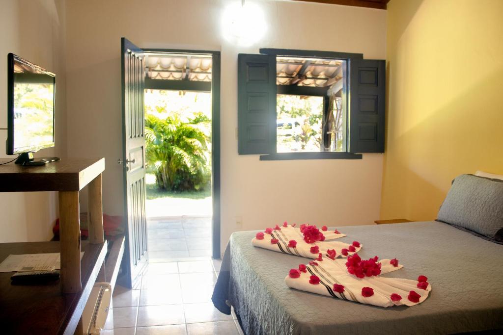 Um quarto na Pousada Lagoa da Pedra com uma cama decorada com cisnes de toalha e pétalas de flores, porta aberta e janela mostrando a vegetação do lado de fora, para representar pousadas em Imbassaí.