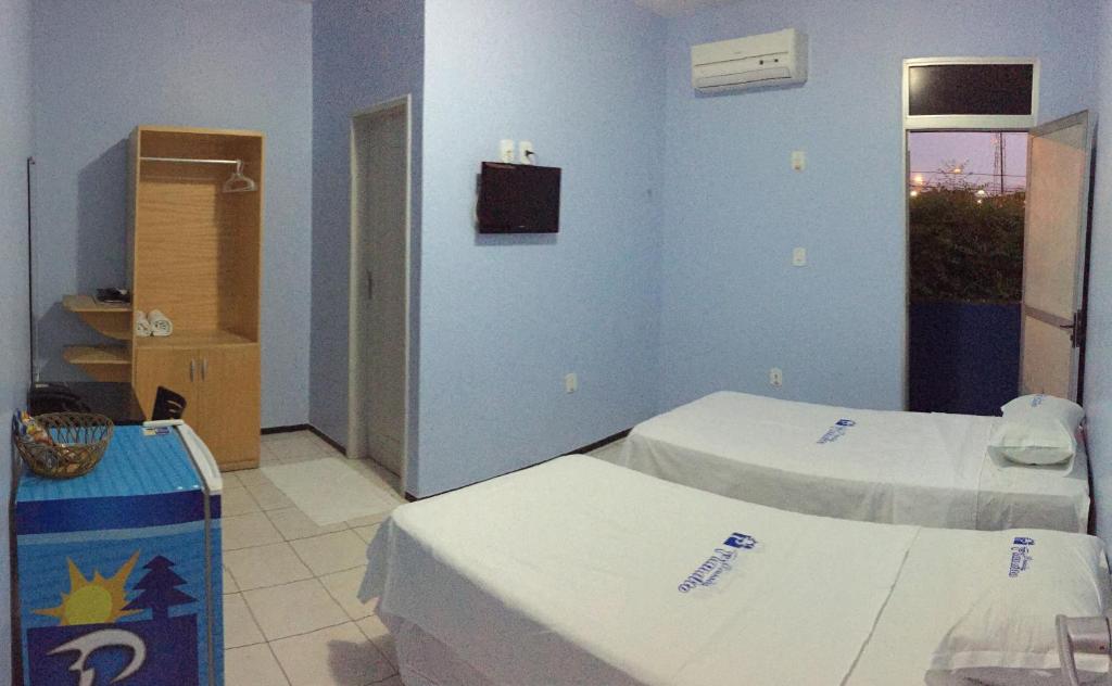Quarto com duas camas de solteiro, tv, ar-condicionado, guarda-roupa, frigobar e porta do banheiro na Pousada Planalto, para representar pousadas em Juazeiro do Norte.