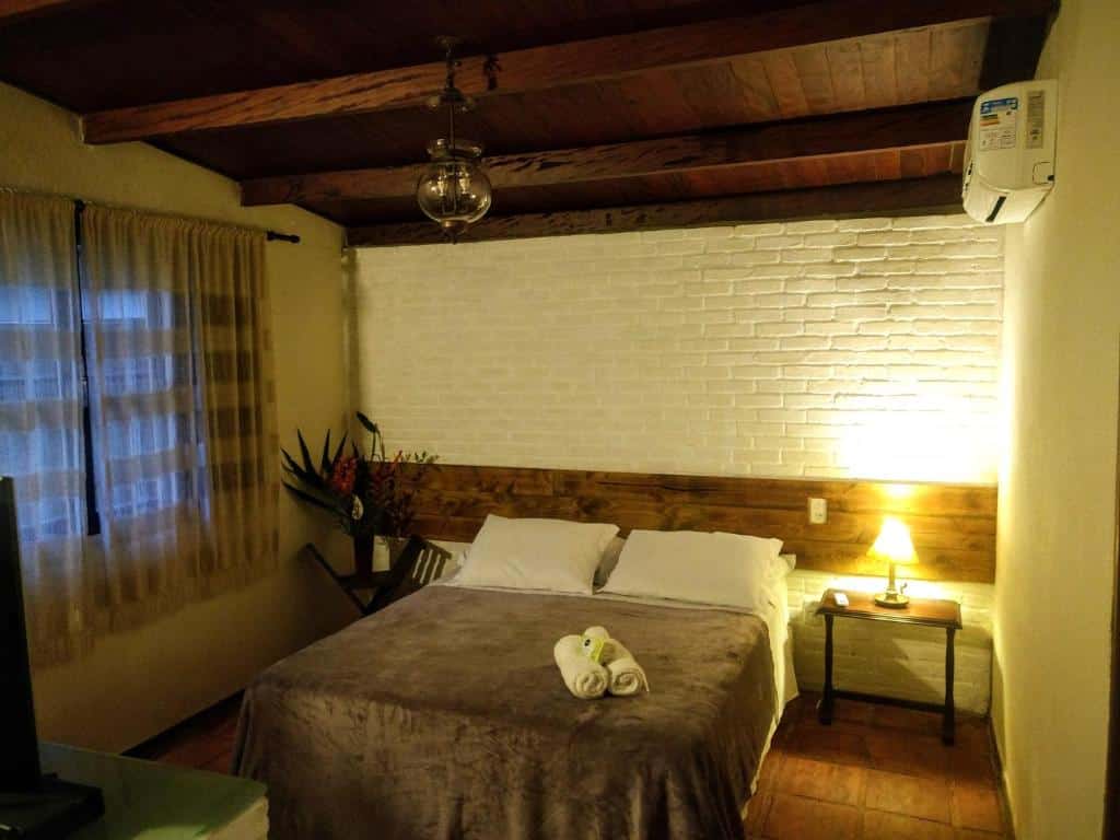 Quarto da Pousada Sítio Itaúna, uma das pousadas em Penedo, com uma cama bem arrumada com toalhas dobradas, uma mesa de cabeceira com uma lâmpada e uma janela com cortinas em um quarto aconchegante.