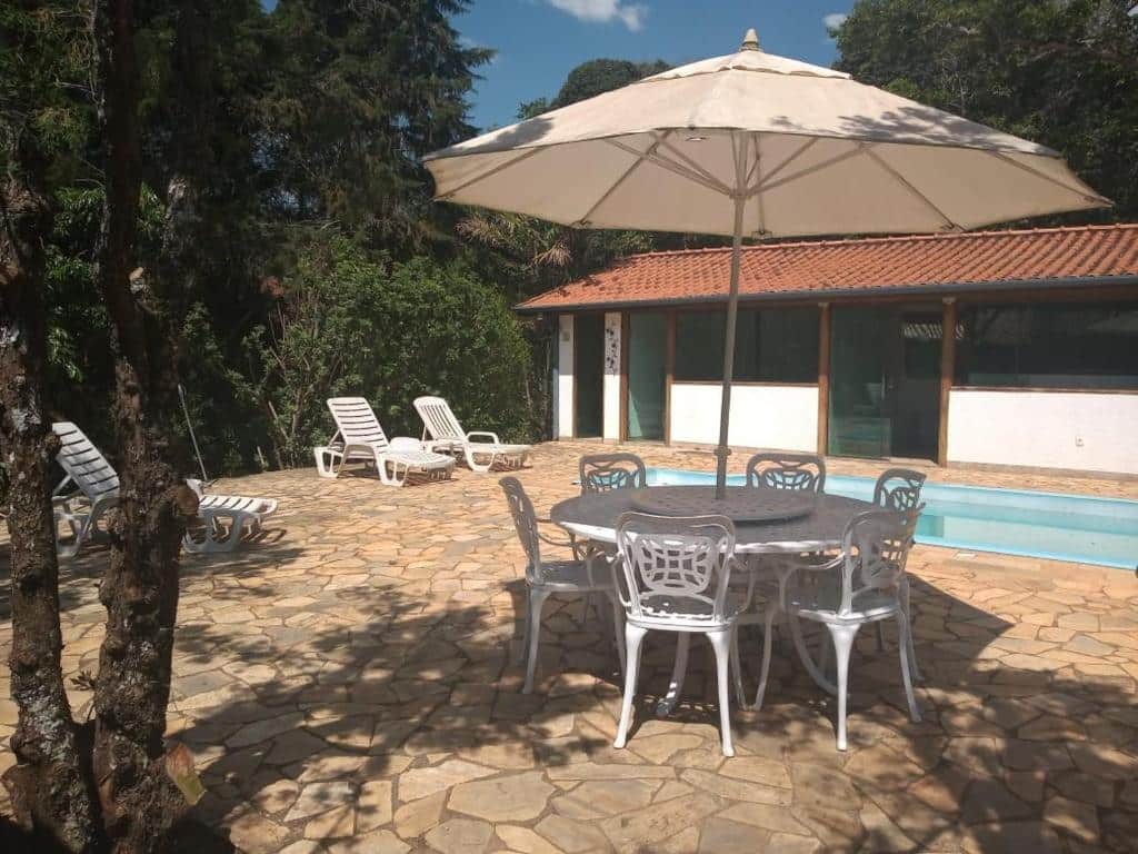 Piscina da Pousada NAIF, com mesas, cadeiras e guarda-sóis ao redor, além de muita vegetação