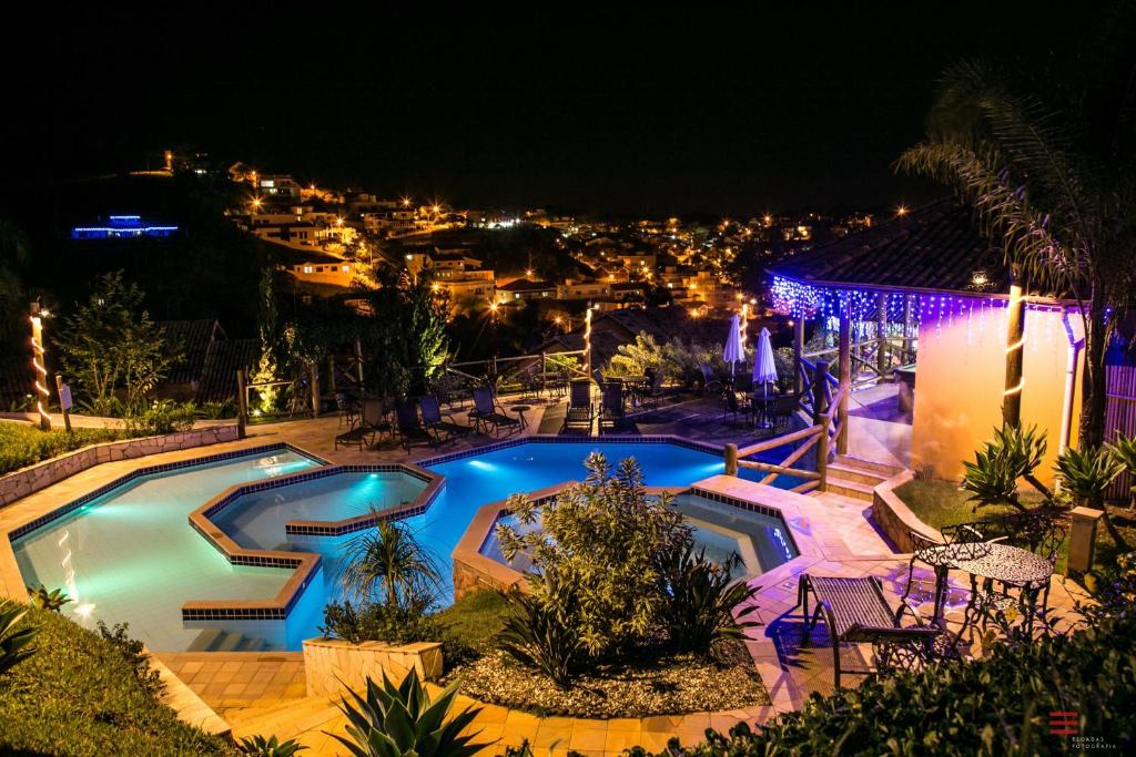 Piscina na Vila Chico, de noite, com luzes coloridas acesas no entorno da piscina e da pousada, com vista para a cidade