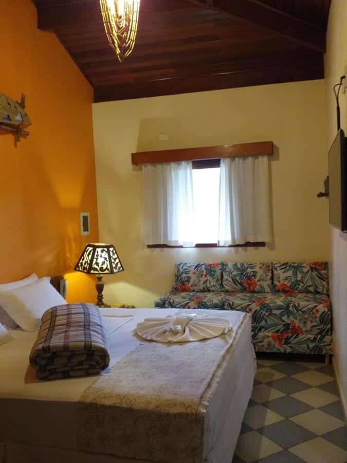 Quarto com cama de casal, abajur, TV e sofá na Pousada Maui