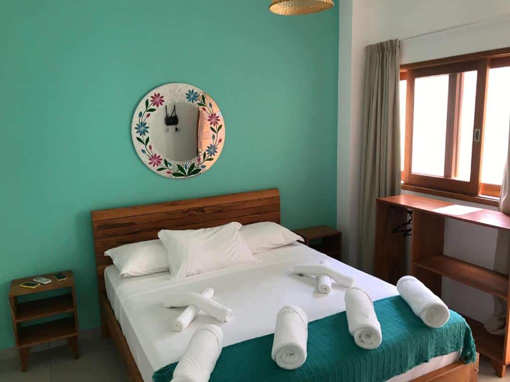 Cama de casal em quarto com parede verde na Nai'a Suites, uma das pousadas em Ubatuba