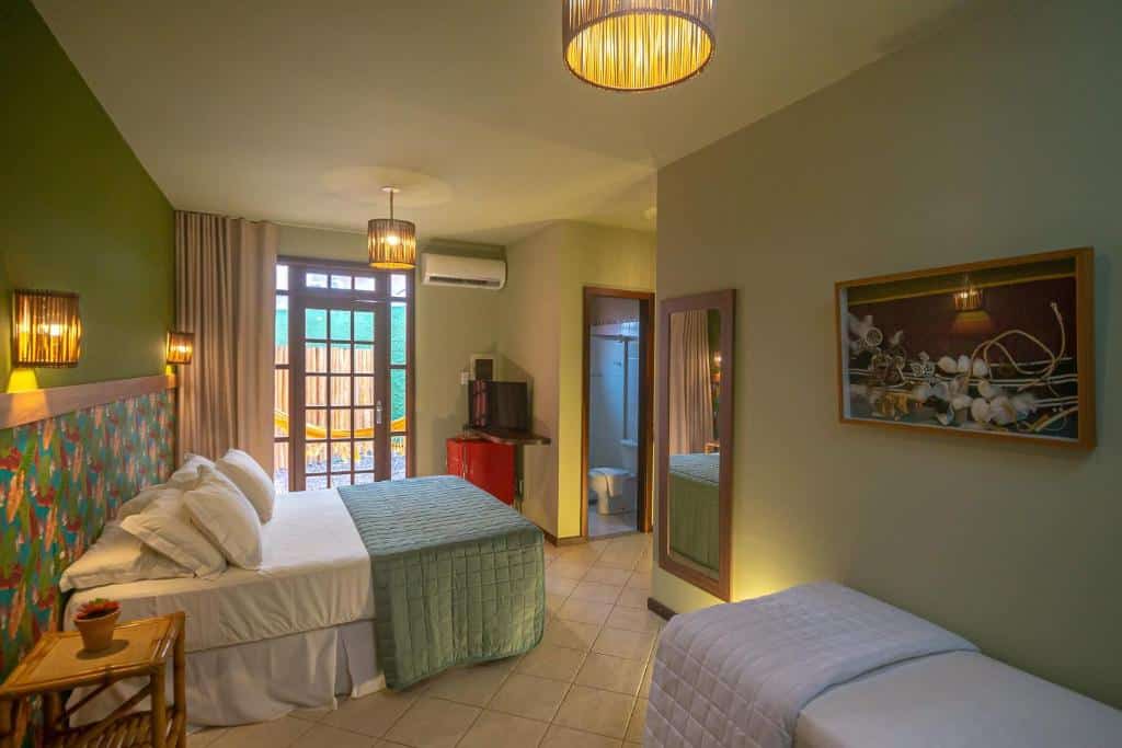 Um quarto na Pousada Villa Maeva em Itacimirim, com uma cama de casal, uma cama de solteiro, arte na parede, TV, espelho e porta que dá para uma varanda ou pátio, para representar pousadas na Linha Verde na Bahia.