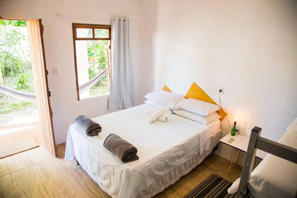 Um quarto arrumado com uma cama de casal, toalhas dobradas, uma pequena mesa de cabeceira, uma janela e uma rede visível do lado de fora, no Mangue Seco Suítes & Bistrô em Mangue Seco, para representar pousadas na Linha Verde na Bahia.
