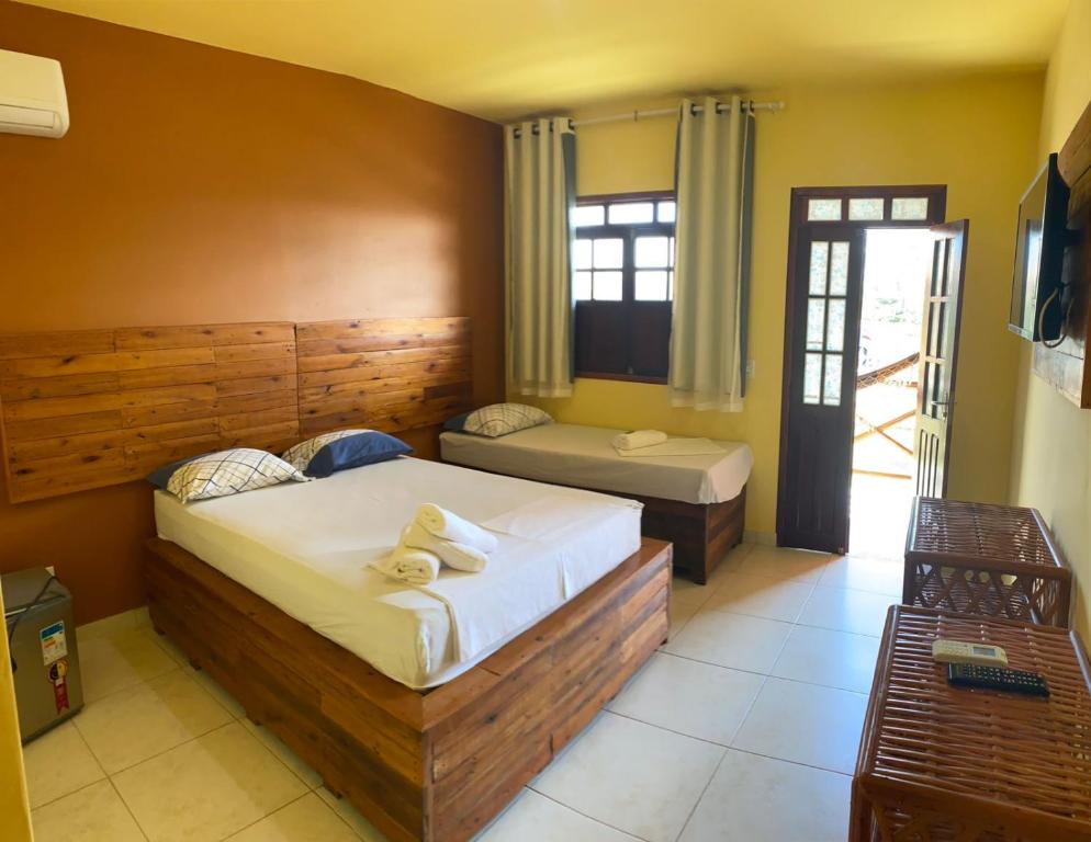 Um quarto na Águas de Sauípe  em Costa do Sauípe, com uma cama de casal, uma cama de solteiro, uma TV, um pequeno frigobar e uma porta que dá para uma varanda, para representar pousadas na Linha Verde em Bahia.