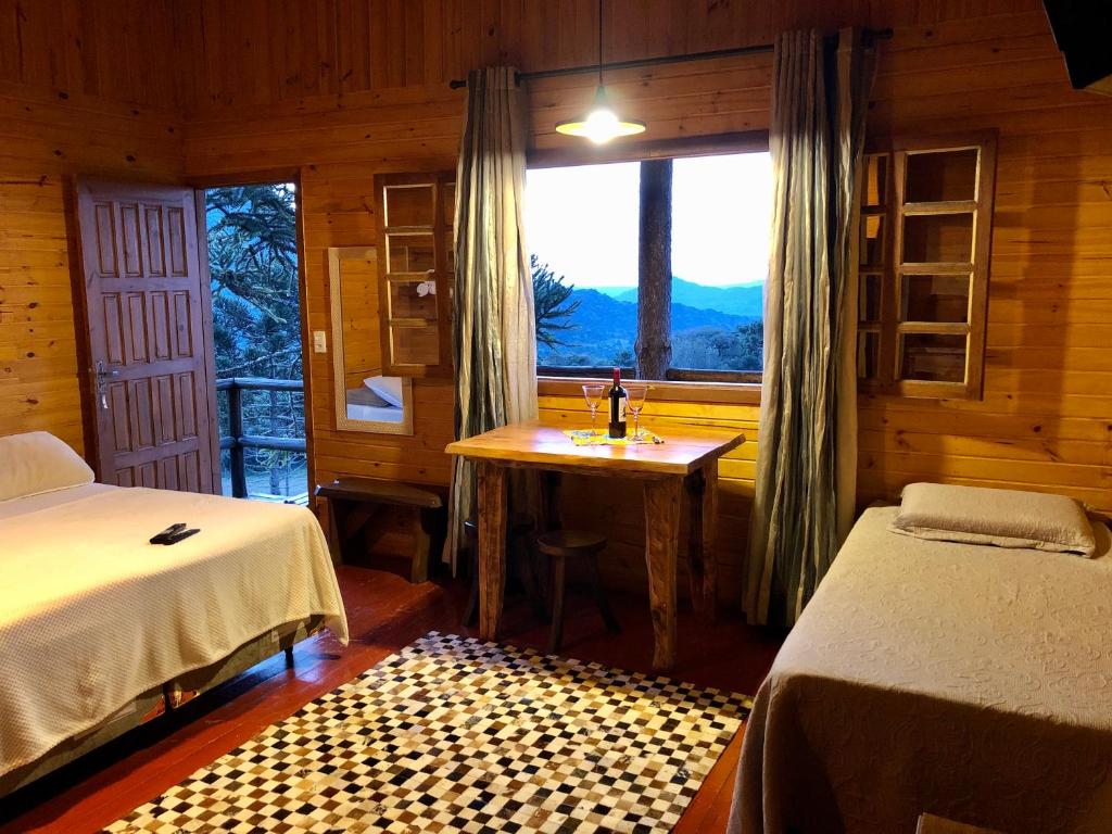 Quarto de madeira aconchegante com duas camas, uma mesa perto de uma janela, uma garrafa de vinho e vista para as árvores e montanhas do lado de fora. Esta é uma das pousadas na serra catarinense.
