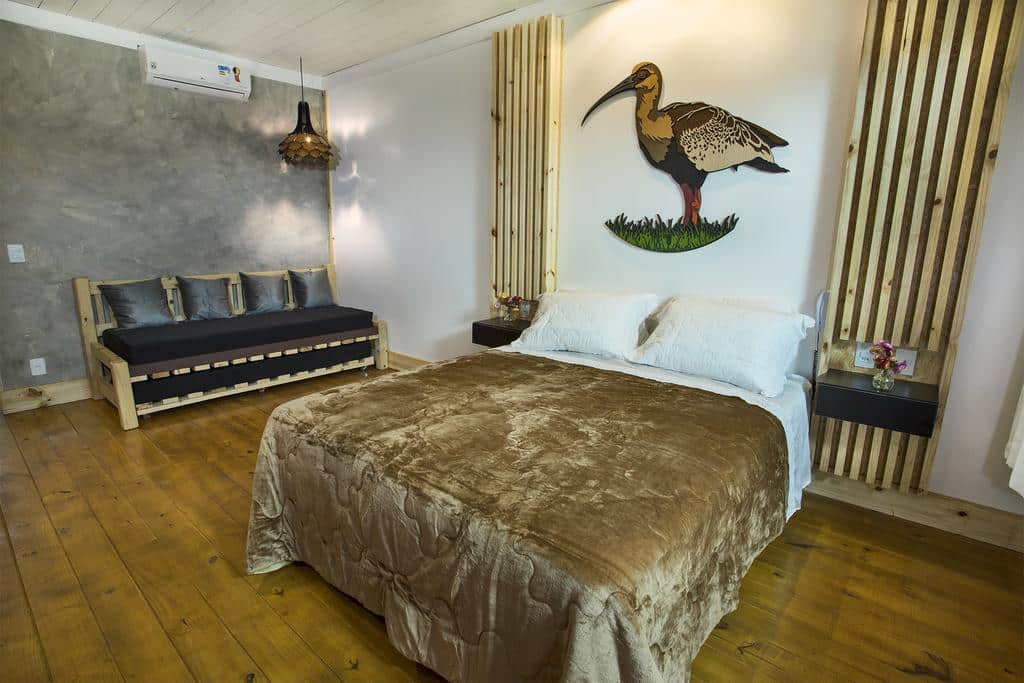 Quarto com cama, sofá, piso de madeira, arte de parede de um pássaro acima da cama e elementos de decoração moderna.