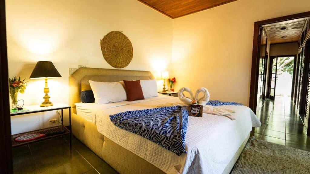 Quarto do Canto das Laranjeiras Beach Club Guaiuba com uma cama de casal grande, mesinhas nas laterais da cama com abajures e vasos e flores, sob a cama há toalhas e almofadas
